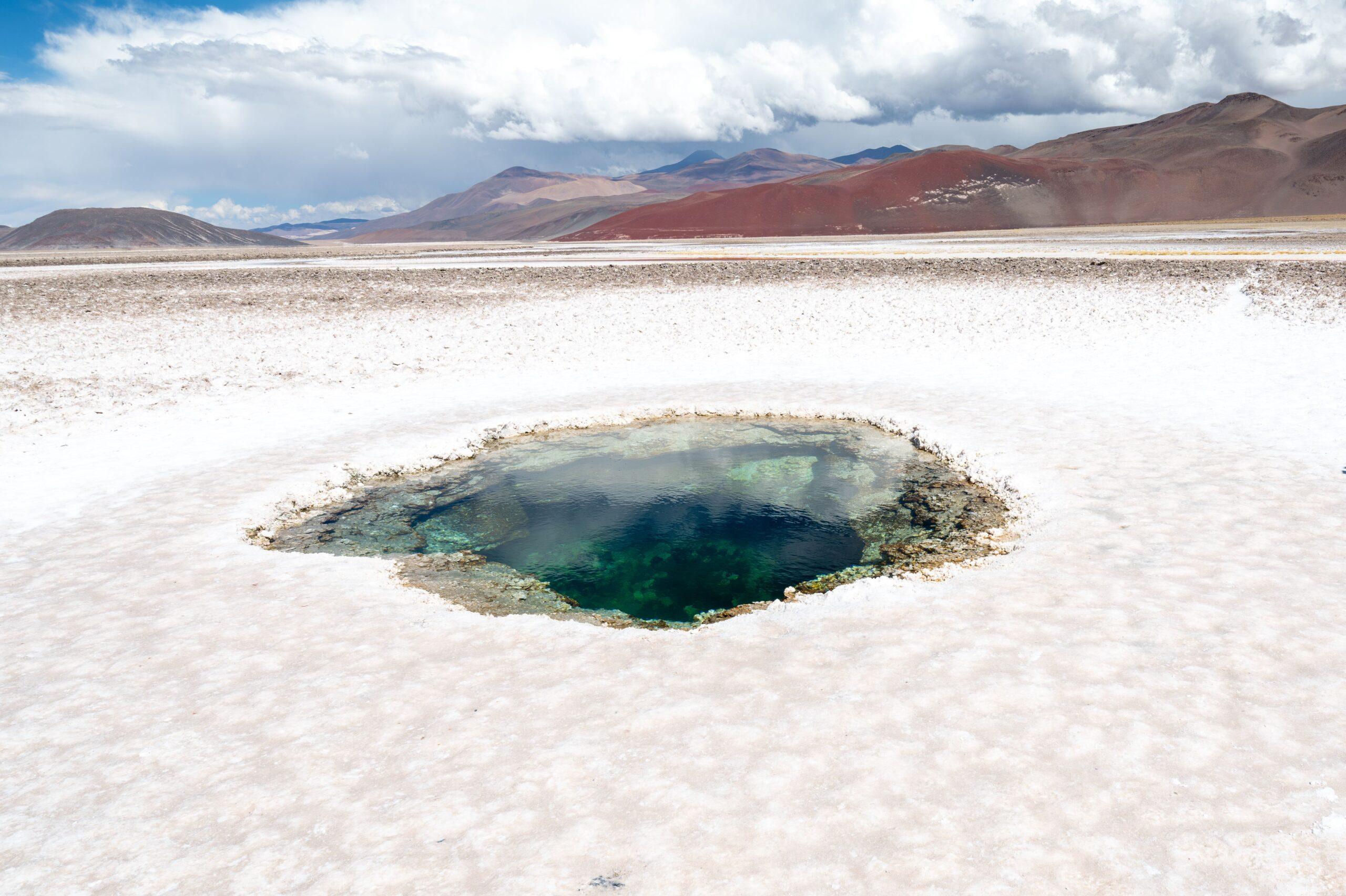 A stunning view of the Ojo de Agua at Salinas Grandes, Catamarca, with vibrant colors and majestic mountains.